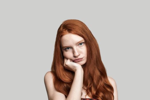 Feeling upset. frustrated girl with red hair making sad face while standing against grey background. Human emotions. Negativity