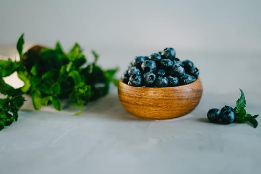A small wooden bowl with berries. Juicy and ripe blueberries in an eco-friendly dish. Sprigs of fresh mint in a kraft bag. The concept of healthy eating and nutrition