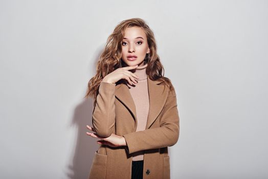 Portrait of young beautiful girl with brown hair, wearing beige coat and turtleneck smiling, looking at camera isolated over white background