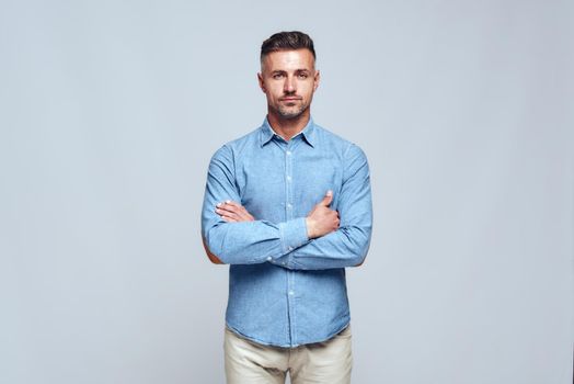 Studio shot of young handsome bearded man in casual wear standing with crossed arms and looking at camera. Fashion look. Men beauty