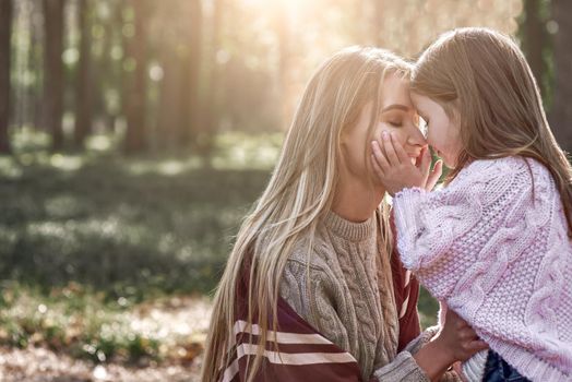 Little girl and her mother in the forest. Woman is wearing a stylish hat and knitted coat, girl is in pink bright sweater