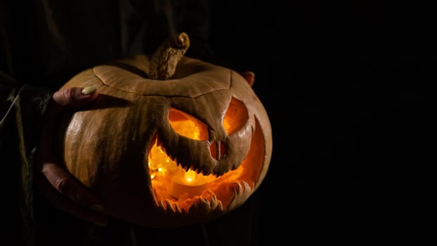 The witch is holding a pumpkin jack o lantern glowing in the dark. Halloween