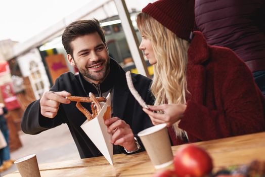 Couple are eating outdoors . Young couple are eating churros at the street food market. Cold season. Close-up photo of couple eating from one package