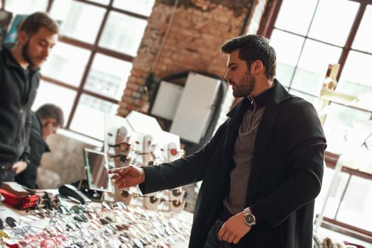 Young stylish man in coat choosing glasses. Customer in street market choosing the eyeglasses from a shelf with many different models