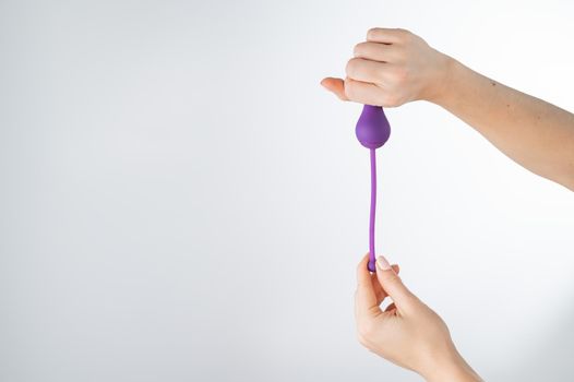 A faceless woman holding an electronic Kegel trainer for training pelvic floor muscles on a white background. Sex toy synchronized with a smartphone.