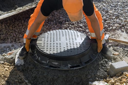 Installing cast iron sewer hatch on a concrete base of installation of water main sewer well in the ground at a construction site