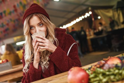 Hot drink at autumn. Close-up of woman drinking mulled wine at the street fair market. Cold season. Close-up photo of blonde woman