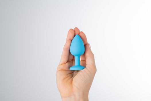 Woman holding a blue anal plug on a white background. Adult toy for alternative sex.