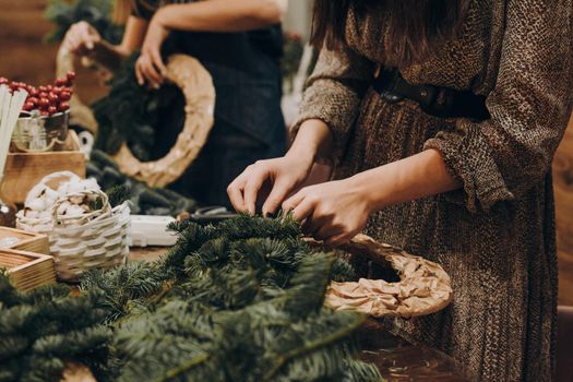 Woman making christmas wreath. Concept of florist's work before christmas holidays. Creating a Christmas wreath of spruce branches and a cardboard frame. Decoration for the house for Christmas.