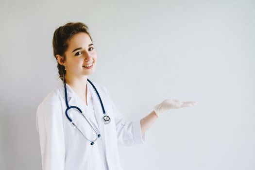 A beautiful doctor girl. A medic on a pure white background. The doctor points to an empty space for text. Doctor with a smile on her face points her hand in a rubber glove to an empty place.