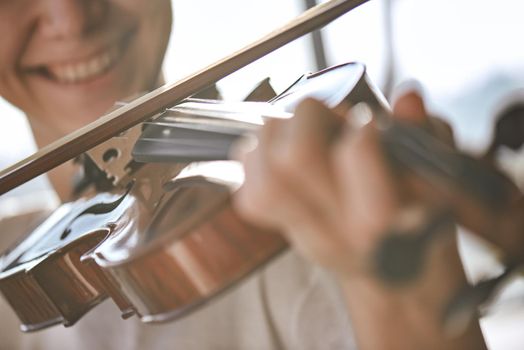 Enjoying classical music. Close up view of smiling violinist playing classical music on the brown wood violin. Musical instruments. Music equipment. Violin lessons