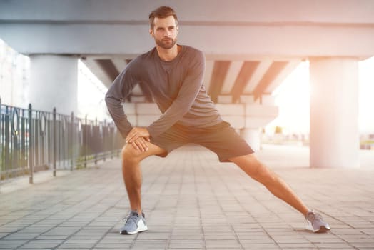 Life is a sport Full-length of young and confident bearded man in sportswear stretching his leg while standing outdoors. Sport concept. Healthy and active lifestyle