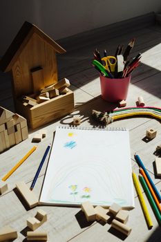 Rainbow of thread and rope and yellow month. Children's drawing in a sketchbook. Cubes are wooden and colored pencils. Pink cup holder. Active game of the child on the floor. Vertical image.