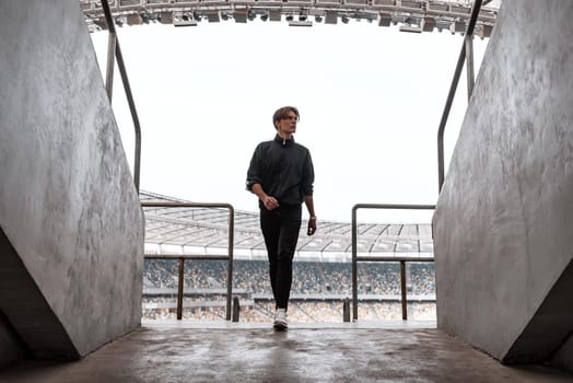 Young sportsman returned from a big empty football stadium . He looks to the right