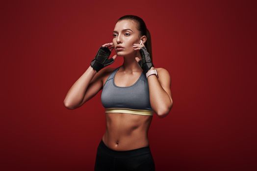 Portrait of pretty sportswoman listening to music using airpods in studio isolated over red background