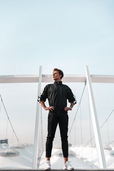 Young sportive man runner posing in full length near the stadium. He looks to the left