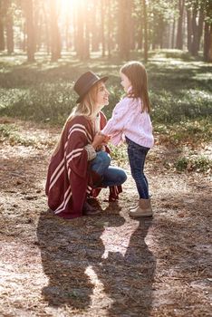 Little girl and her mother in the autumn park. Woman is wearing a stylish hat and knitted coat, girl is in pink bright sweater