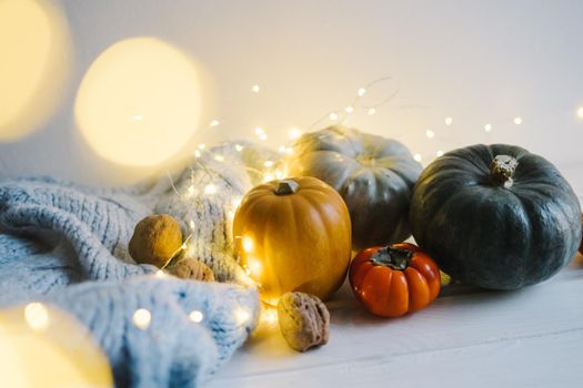 Thanksgiving, Christmas and New Year's Day. Autumn festive composition of garland, pumpkin, nuts, persimmons, red leaves. Wooden house for storage of small things. Blue warm knitted blanket.