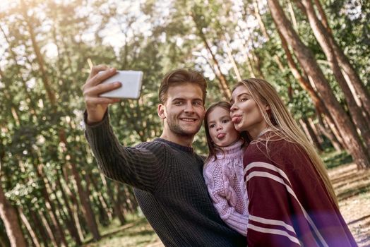 Happy family taking selfie by smartphone in woods. Father is holding smart phone with camera