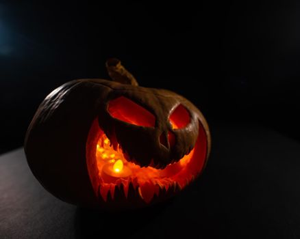 A creepy pumpkin with a carved grimace glows. Jack on a lantern in the dark