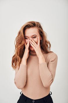 Portrait of sweet gorgeous lady with brown hair, wearing beige turtleneck, she is laughing, almost crying from happiness, looking away, standing isolated over white background