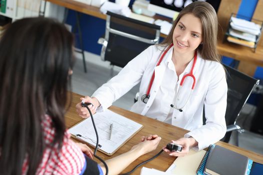 Young female doctor measures blood pressure to a patient. Preliminary health examination before visiting the clinic, health card