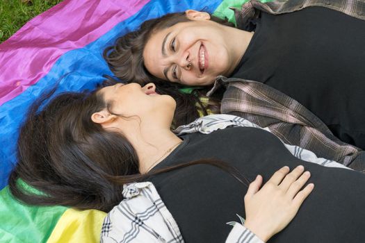 Lesbian couple wearing a lgbt rainbow flag lying on the floor. Affectionate moment between two women under a gay flag. High quality photo.