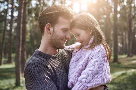 Little girl and her father in the forest. Girl is looking to the father. Young man is wearing a dark sweater, girl is in pink bright sweater