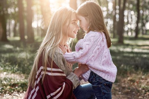 Little girl and her mother in the autumn park. Woman is wearing a stylish hat and knitted coat, girl is in pink bright sweater