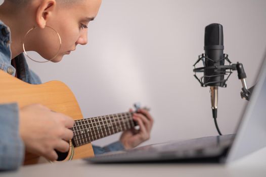 Young caucasian woman with short blonde hair playing guitar and streaming live on laptop