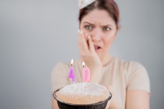 Unhappy woman holding a cake with candles for her 40th birthday. The girl cries about the loss of youth