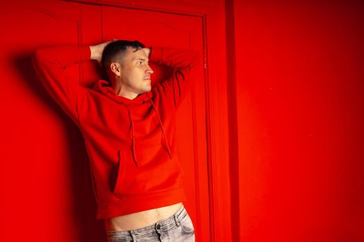 Young handsome man posing near red wall. Attractive male in red hoodie on red background