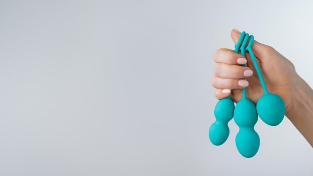 A faceless woman demonstrates a set of mint-colored vaginal balls. Girl holding a kegel trainer for training pelvic floor muscles on a white background