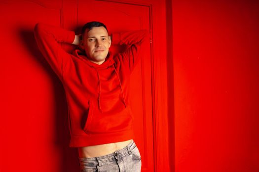 Young handsome man posing near red wall. Attractive male in red hoodie on red background