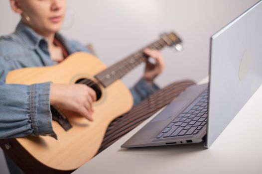 Young caucasian woman with short blonde hair playing guitar and watching training video on laptop