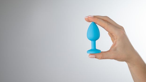 Woman holding a blue anal plug on a white background. Adult toy for alternative sex.