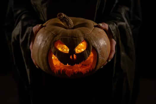 The witch is holding a pumpkin jack o lantern glowing in the dark. Halloween