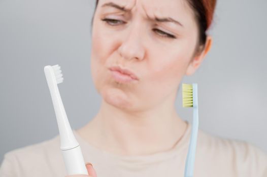 Happy woman compares a toothbrush with an electric one. The girl chooses oral hygiene products.