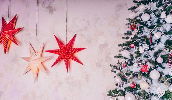 Decorated Christmas tree in the room. Coniferous tree with white and red baubles located near the white wall during the celebration of the holiday.