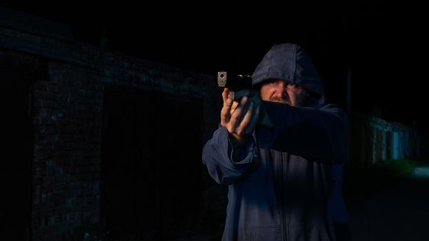 Caucasian man in a hood shoots a pistol