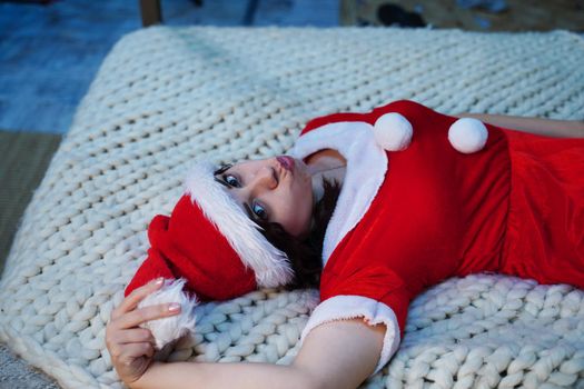 Young woman in Santa costume lying on bed. Charming female resting and celebrating Christmas at home. Concept of holidays and good mood