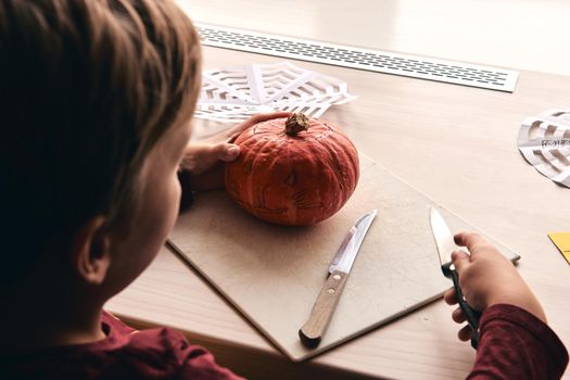 Halloween, decoration and holidays ideas- close up of kid with knife carving pumpkin or jack-o-lantern. 6 years boy has homefamily fun activity. Mom spending time with son together.