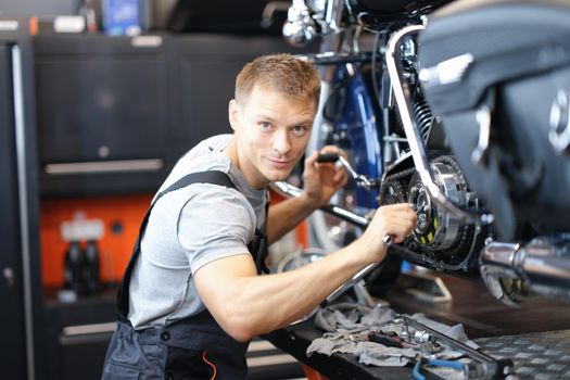 A male mechanic in uniform in a garage repairs a motorcycle. Inspection and diagnostics of a motorbike before the race