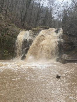 Beautiful landscape of powerful muddy waterfall in mountainous terrain. Dirty mountain waterway flows down and splashes