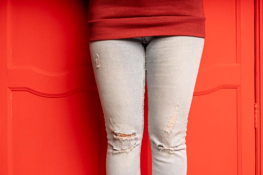 Close up of women's legs in jeans with holes on red background. Fashionable holes in jeans on unrecognizable female