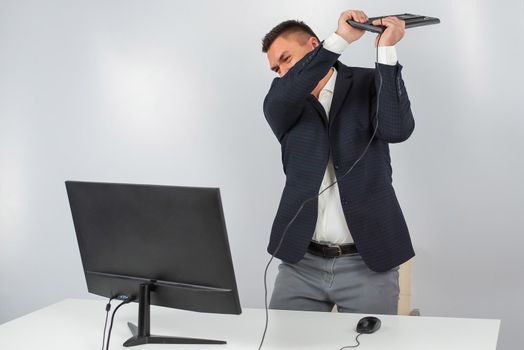 Caucasian man in a suit gets angry and smashes the keyboard on the monitor. An office worker in a rage breaks the computer