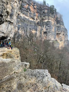 Tourists on huge cliff with spectacular view of nature. Group of people on high rock in foggy and cloudy weather.