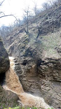 Beautiful landscape of powerful muddy waterfall in mountainous terrain. Dirty mountain waterway flows down and splashes