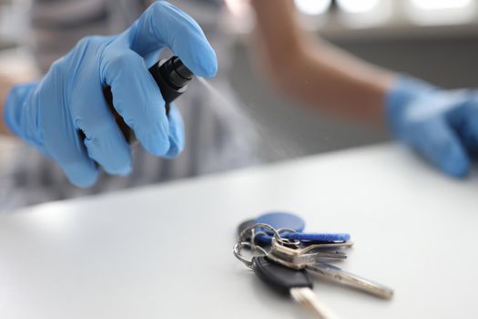 Hands in gloves treat keys on the table with a sanitizer, close-up. Antibacterial antiviral spray, virus protection during pandemic