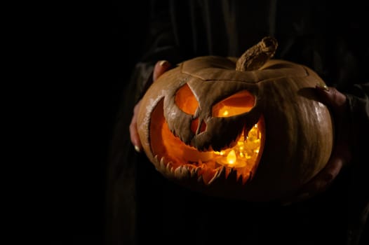 The witch is holding a pumpkin jack o lantern glowing in the dark. Halloween